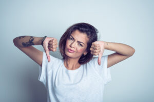Portrait of disappointed young woman standing with thumbs down